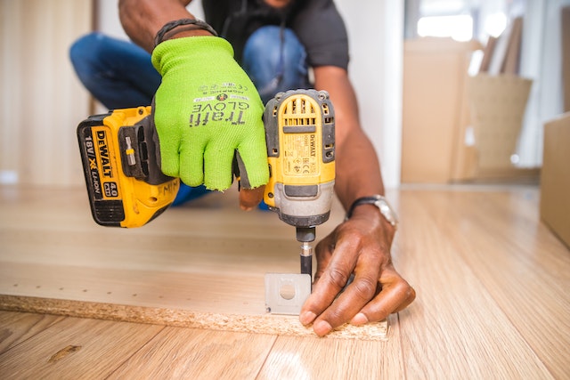 person with a green work glove using a power drill on a piece of wood
