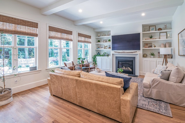white living room with wood flooring a tan couch and three large windows