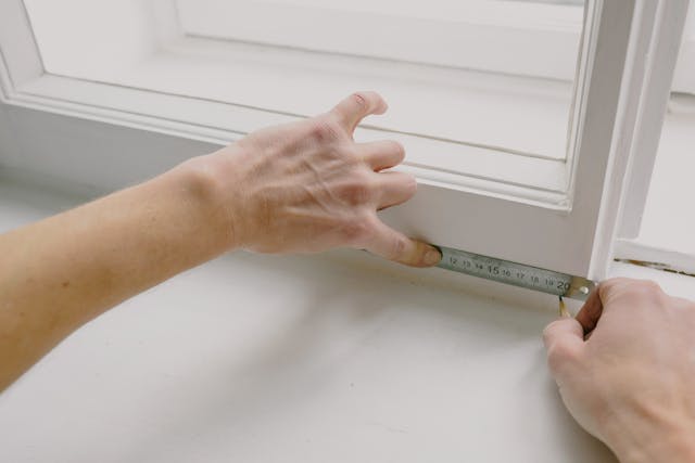 someone measuring a window pan with a tape measure